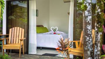 Una habitación con una cama, dos sillas de madera y un ventanal de vidrio que da a un jardín.