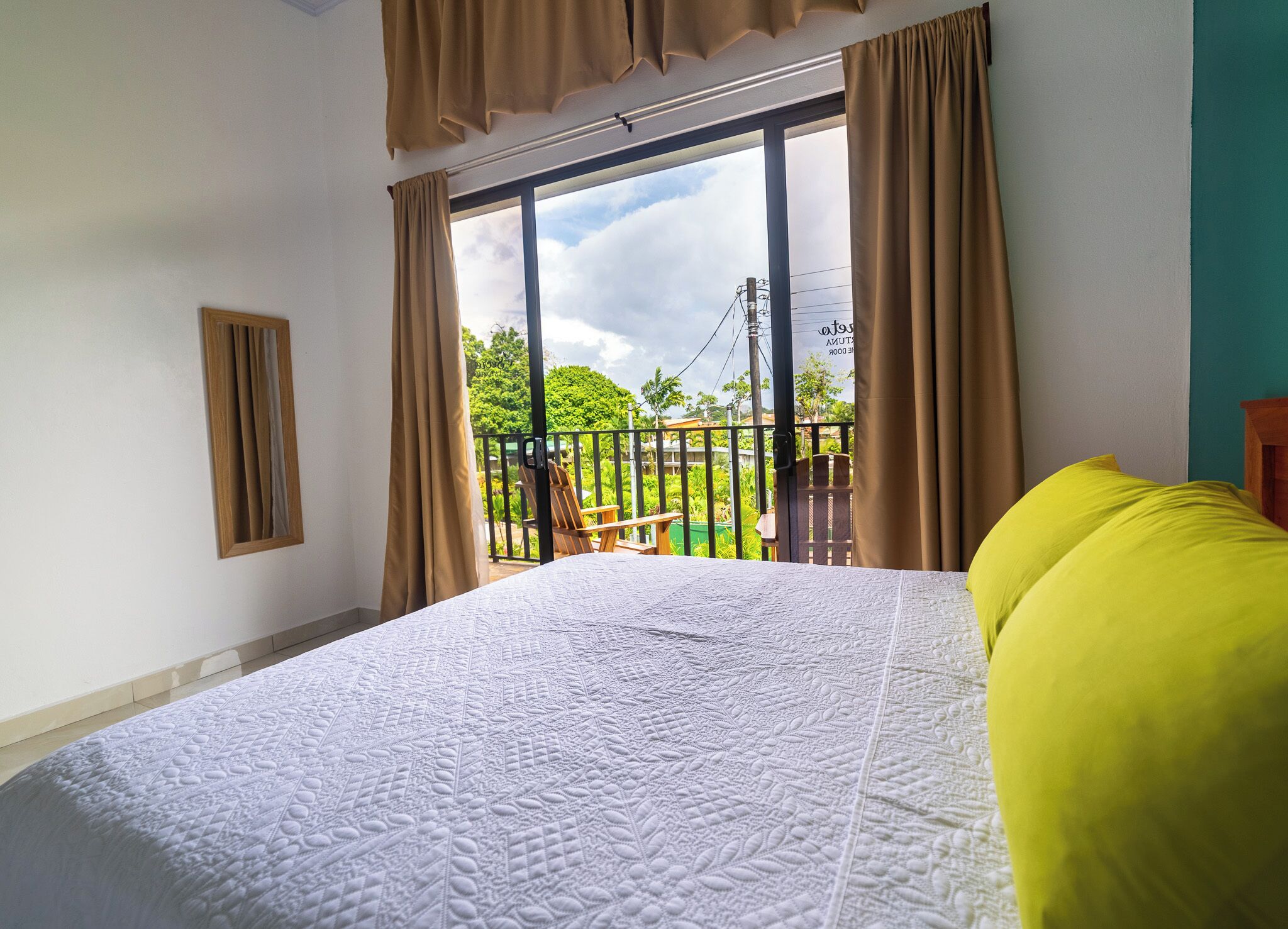 A bedroom with a large bed, a balcony with a chair, and a view of greenery.