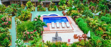 Vista aérea de un resort con piscina central, rodeado de exuberante vegetación y palmeras.