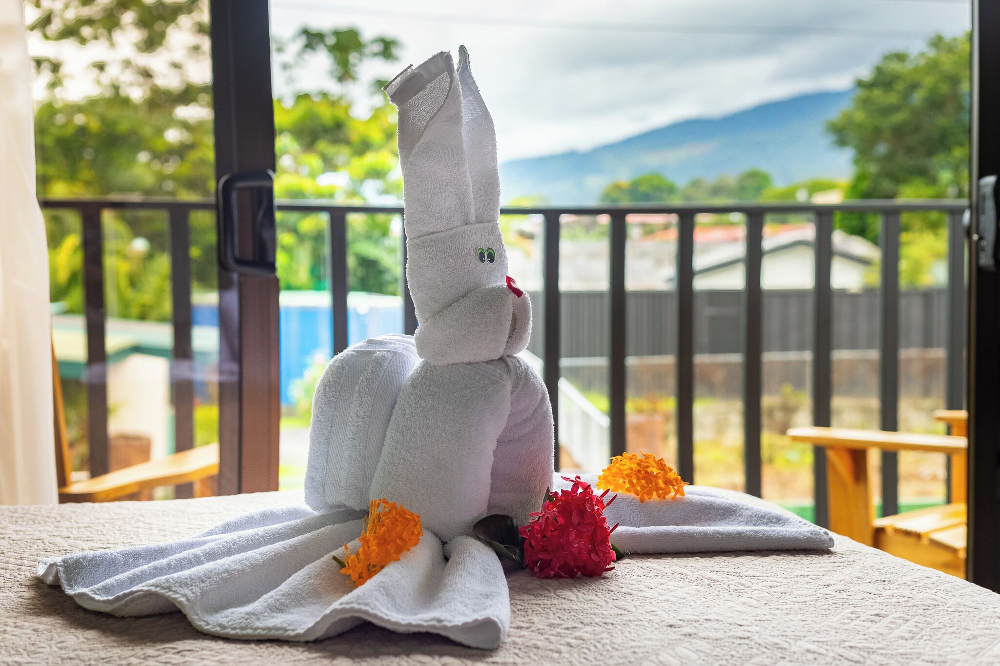 A towel sculpture on a bed with a view of a balcony and outdoor scenery.