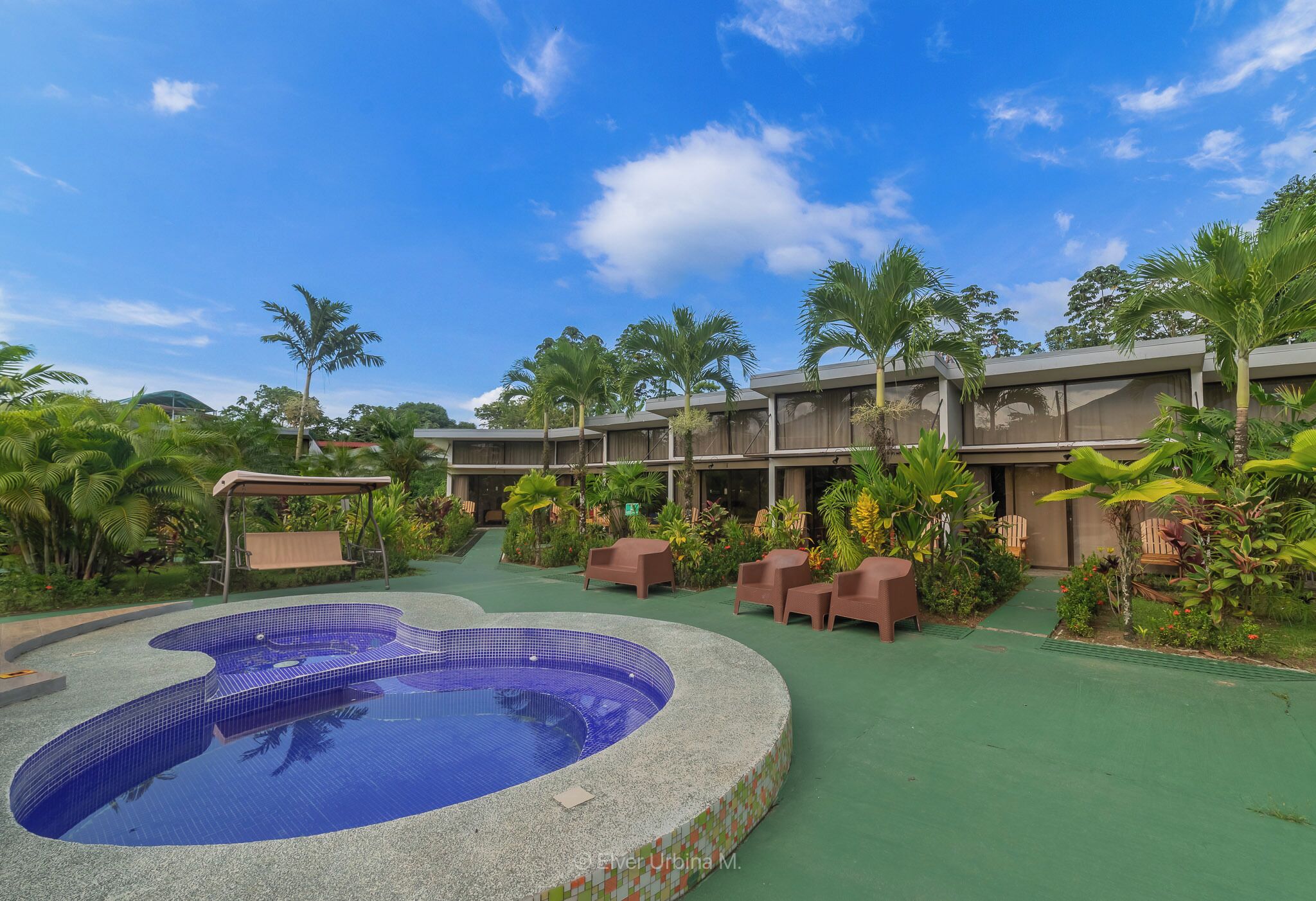 A swimming pool with a tiled edge, surrounded by greenery and a covered seating area.