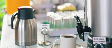 Una estación de café con una cafetera, una taza de café negro, un vaso de jugo de naranja y un cartel que dice 'Café negro Black coffee'.