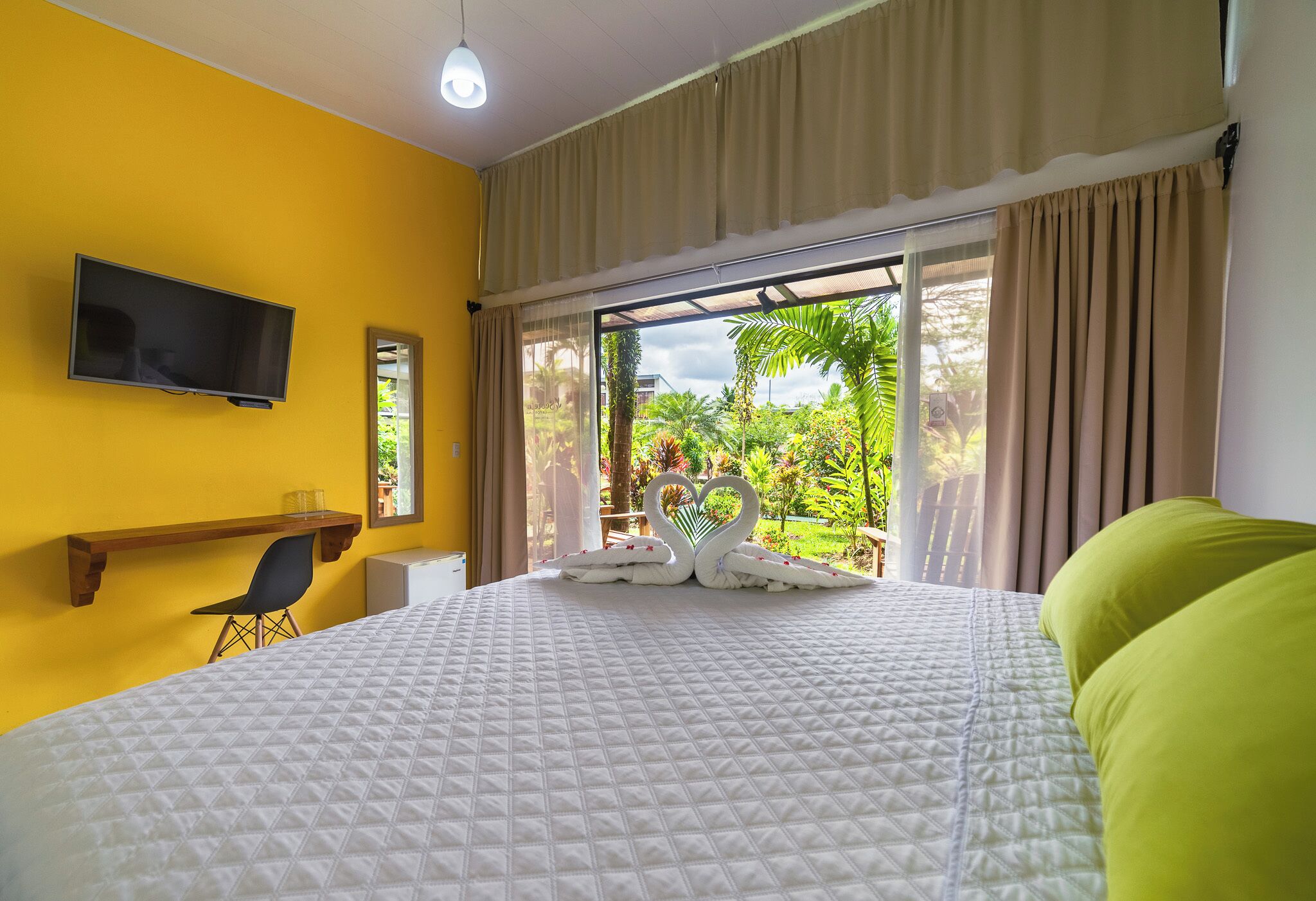 Habitación de hotel con cama, televisión montada en la pared, escritorio con silla y ventana con cortinas.