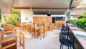 A spacious outdoor dining area with wooden tables and chairs, a tiled floor, and a wooden wall with a logo. - Hotel Secreto La Fortuna (La Fortuna)