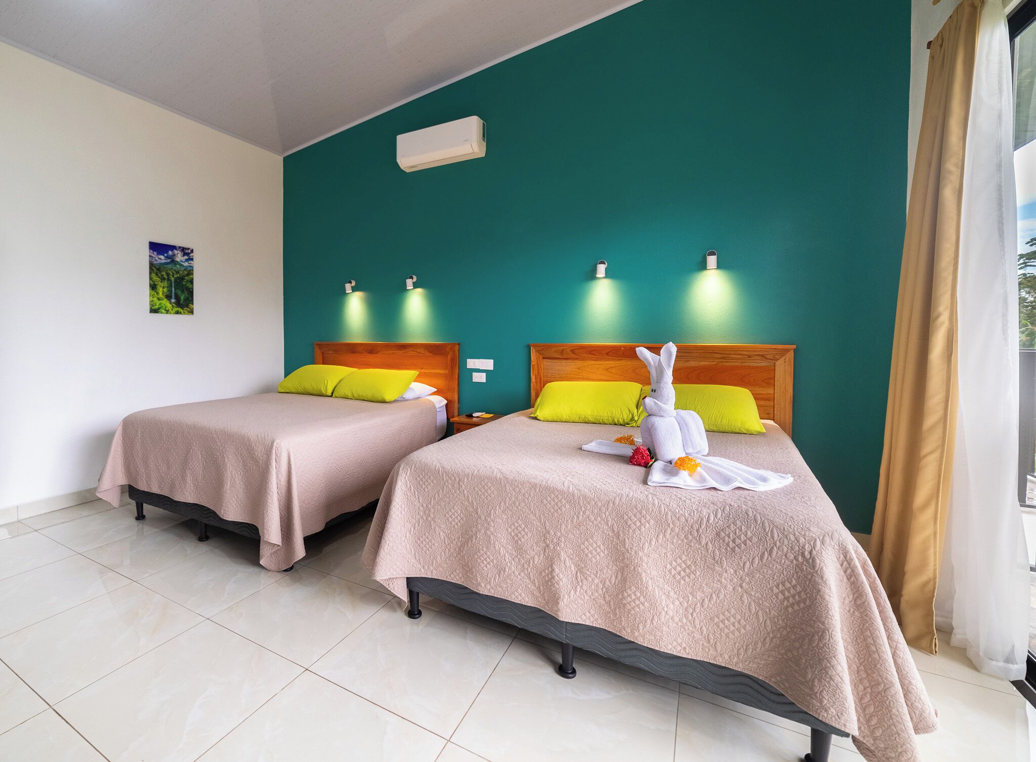 Deux lits simples avec des têtes de lit en bois, des murs de couleur turquoise et une fenêtre avec des rideaux.