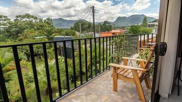 Un balcon doté d’un sol en pierre, de meubles en bois et offrant une vue sur un jardin luxuriant et des montagnes.