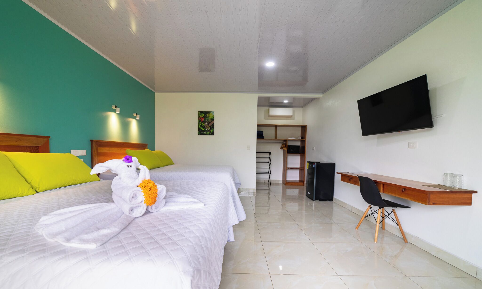 A hotel room with two beds, a desk, a TV, and a bathroom visible in the background.