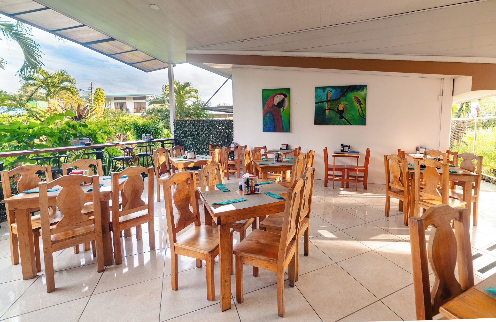 A restaurant with wooden tables and chairs, a tiled floor, and paintings on the wall.