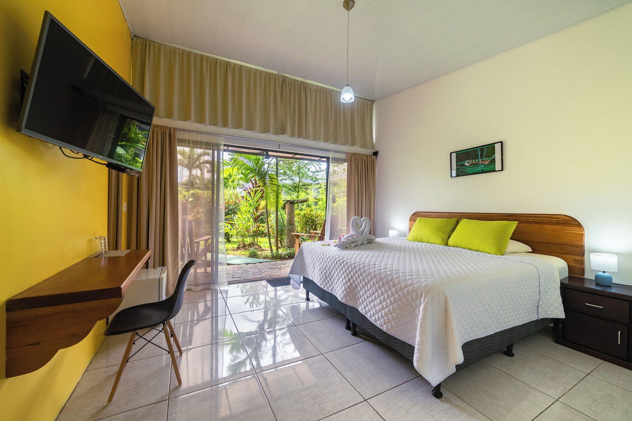 Une chambre d’hôtel équipée d’un lit, d’un bureau, d’une chaise, d’une télévision et offrant une vue sur la verdure environnante.