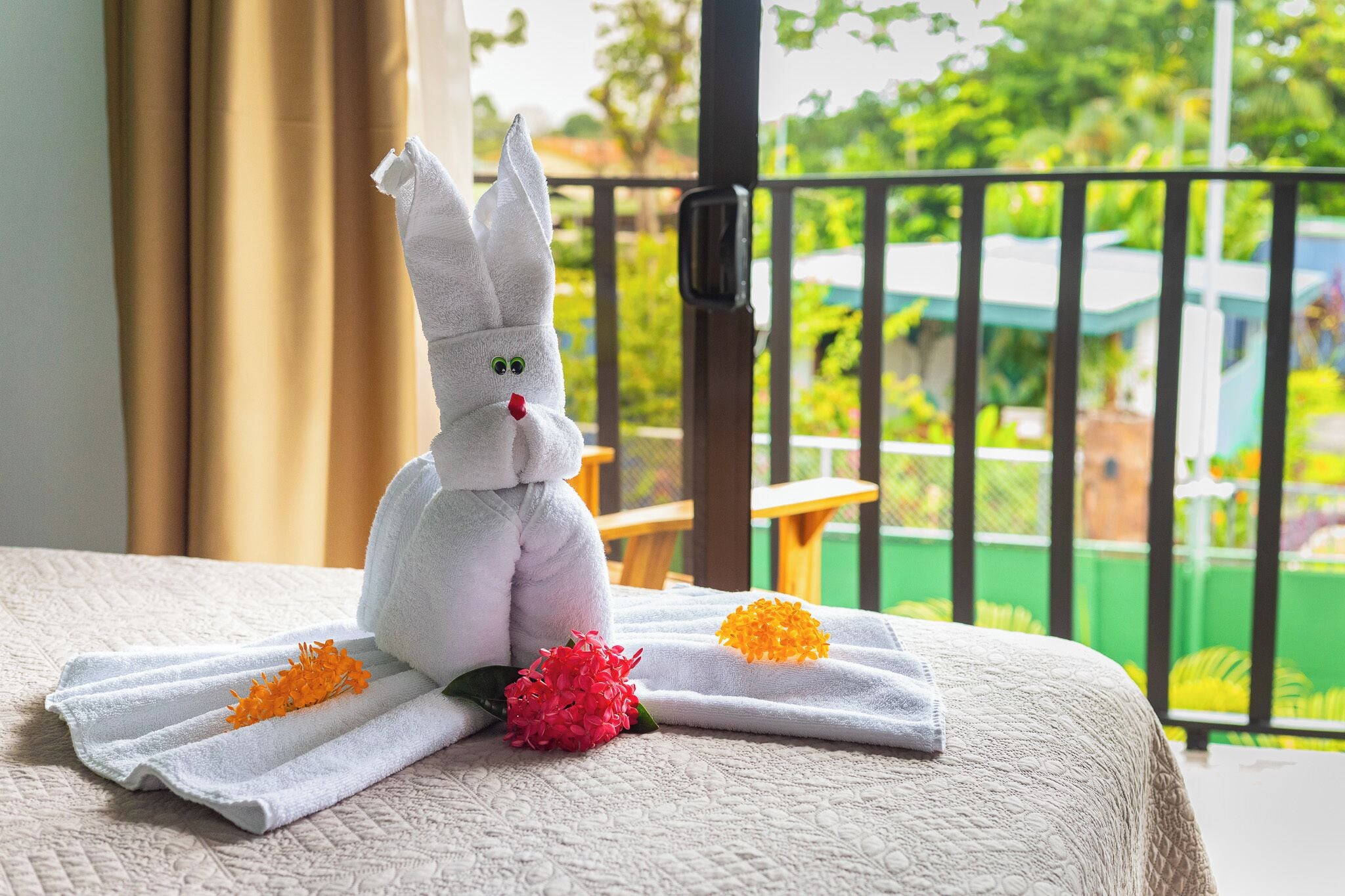 A white towel with a bunny figure and two flowers on a bed.