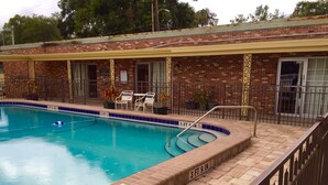 Una piscina con borde de ladrillo, cubierta de baldosas y cercada.