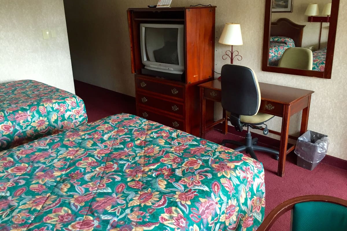 Une chambre d’hôtel avec deux lits, un bureau, une chaise, une télévision et un miroir.