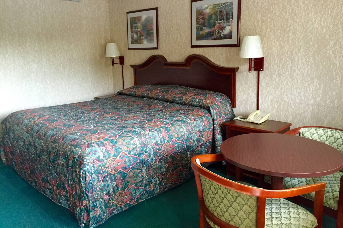 Une chambre d’hôtel avec un grand lit, deux lampes de chevet, une petite table avec une chaise et deux tableaux encadrés au mur.