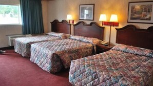 Habitación de hotel con tres camas, cada una con colcha estampada, lámpara de noche y un cuadro en la pared.