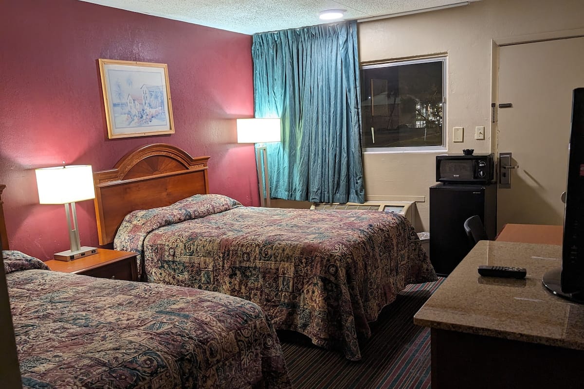 Une chambre d’hôtel avec deux lits, un bureau, une télévision et une fenêtre avec des rideaux.