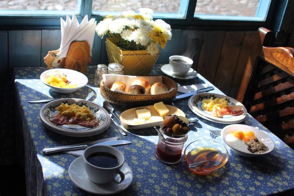 A breakfast table with various dishes, a vase of flowers, and a window view.