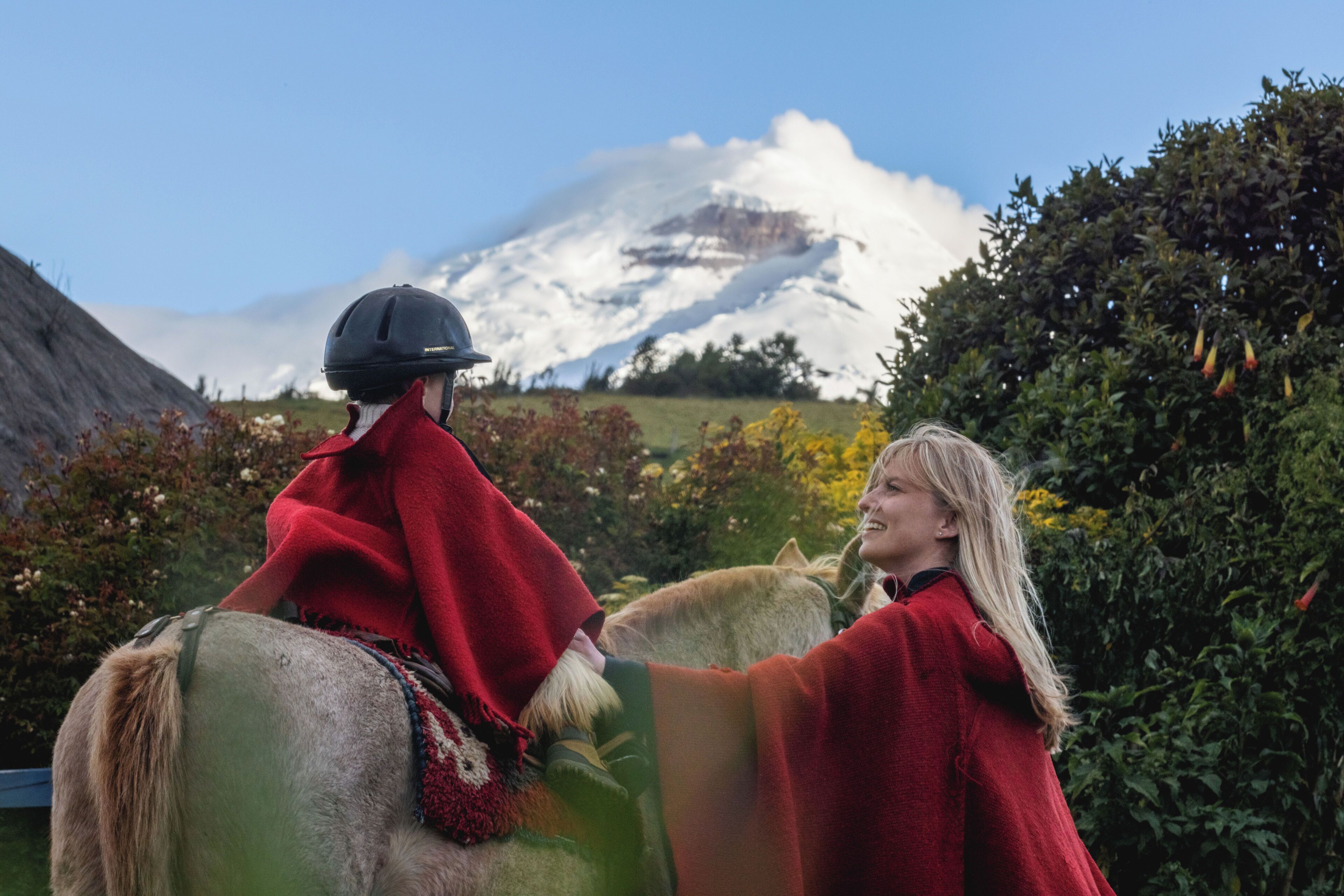 Een persoon te paard, met een rode deken, een andere persoon in een rode mantel, en een berg op de achtergrond.