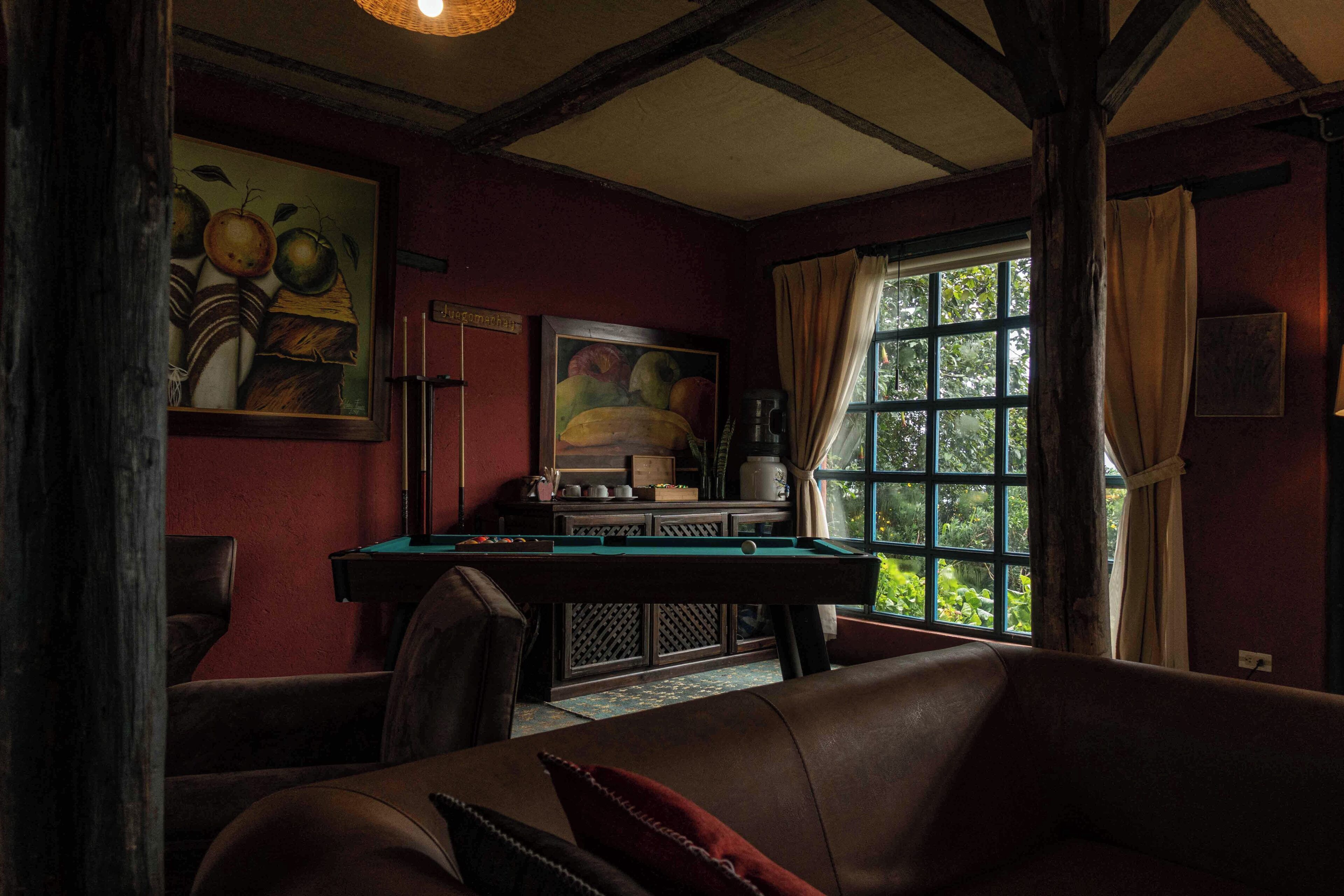 Une pièce avec une table de billard, un canapé, un tableau et une fenêtre avec des rideaux.