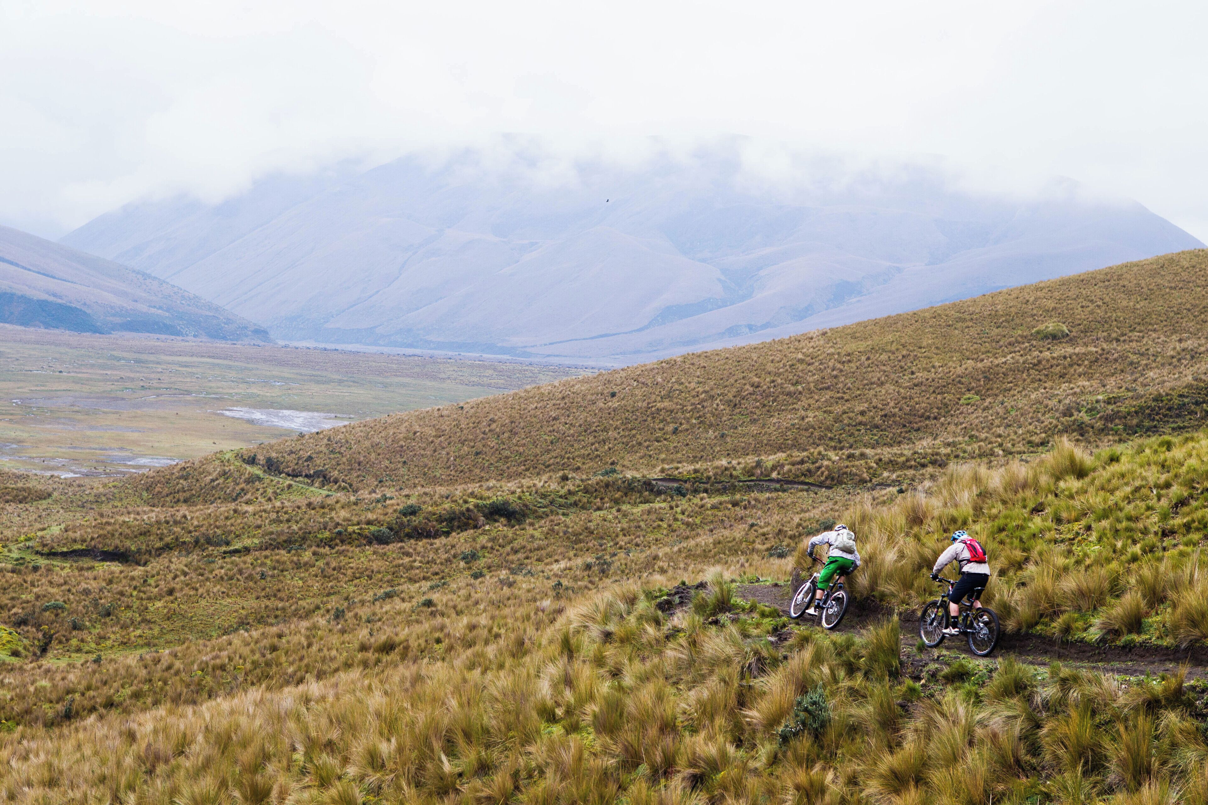 A mountainous landscape with two cyclists on a trail.