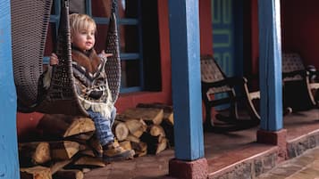 Un niño en un columpio, una pila de leña y sillas mecedoras.