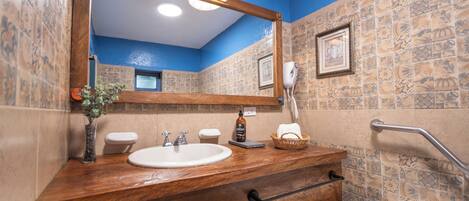 Une salle de bain avec un meuble-lavabo en bois, un évier, un miroir, un porte-serviettes, un sèche-mains et un espace douche.
