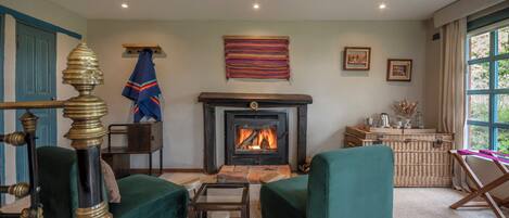 Una sala de estar acogedora con chimenea, sillones tapizados en verde, una mesa de centro de madera y una mesita auxiliar de mimbre.