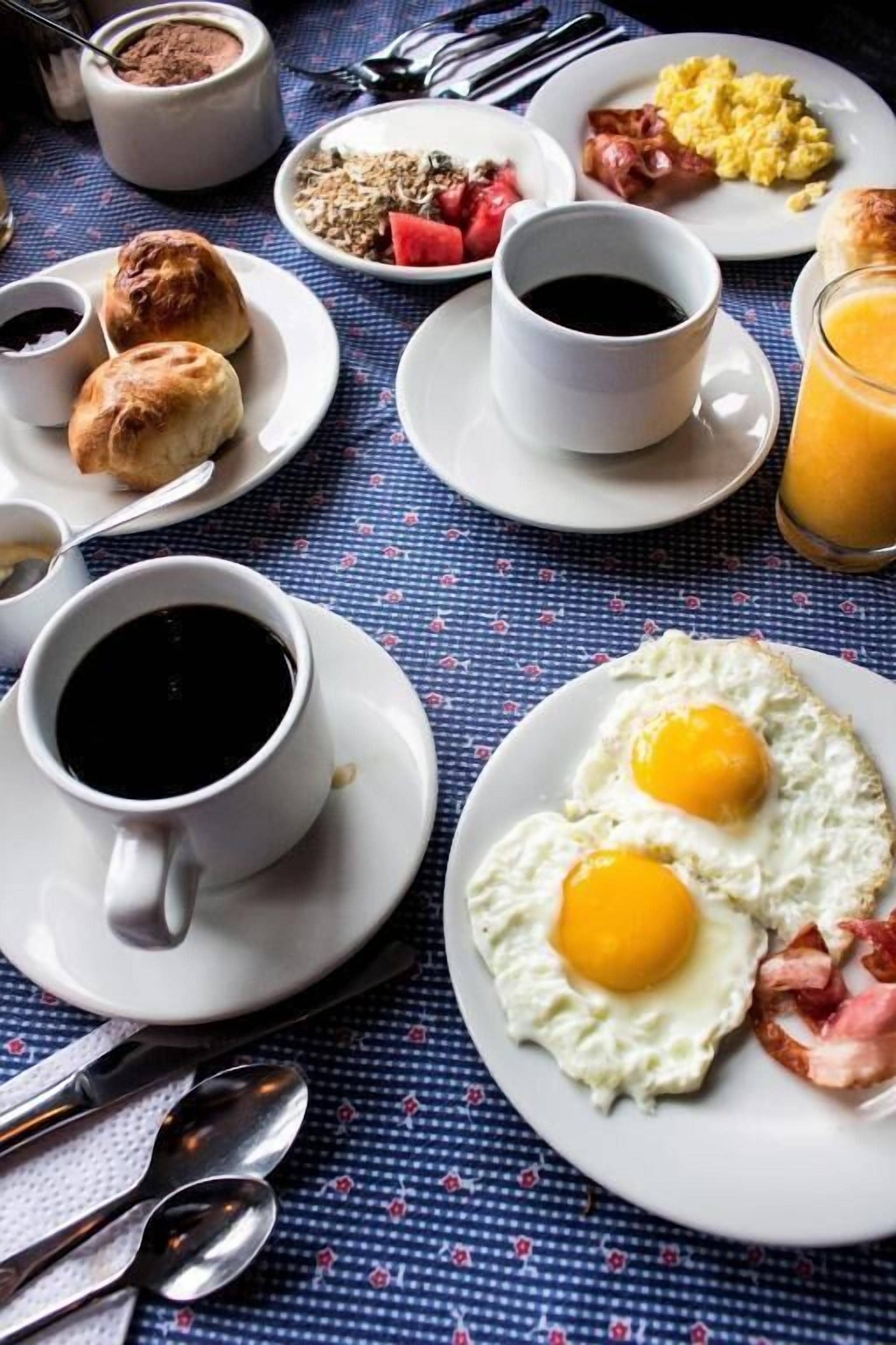 Ein Frühstückstisch mit Eiern, Speck und Toast, dazu Kaffeetassen und Saft.