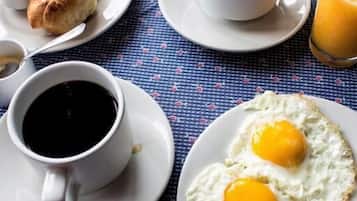 Una mesa de desayuno con platos de huevos, tocino y tostadas, además de tazas de café y jugo.