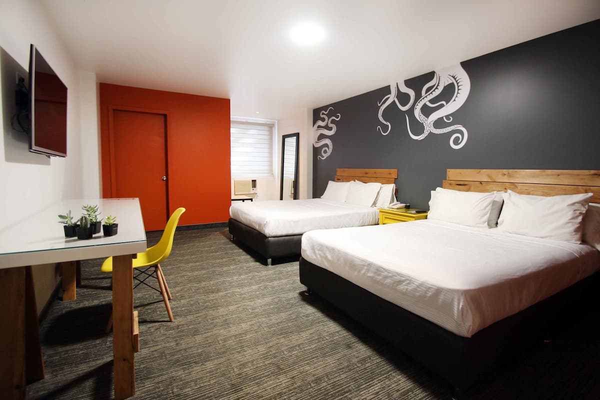 A hotel room with two beds, a desk with a chair, a TV, and a wall with a decorative design.
