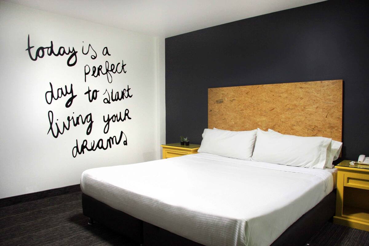 A neatly made bed in a hotel room with a motivational quote on the wall.