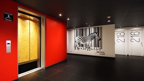 Un vestíbulo moderno de hotel con una pared roja, un ascensor y un mural de cebra.