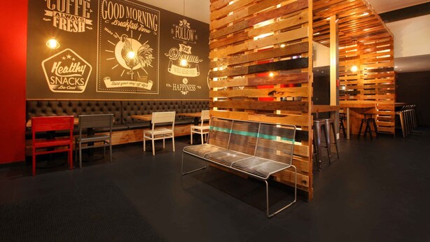 Interior moderno de una cafetería con pared de listones de madera, asientos cómodos y decoración con mensajes inspiradores.