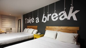 Habitación de hotel con dos camas, un cabecero de madera, una mesita de noche con teléfono y una pared que dice 'Take a break'.
