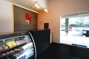 Uma área de recepção de hotel com um expositor de vidro de lanches, um balcão de recepção e vista para o estacionamento.