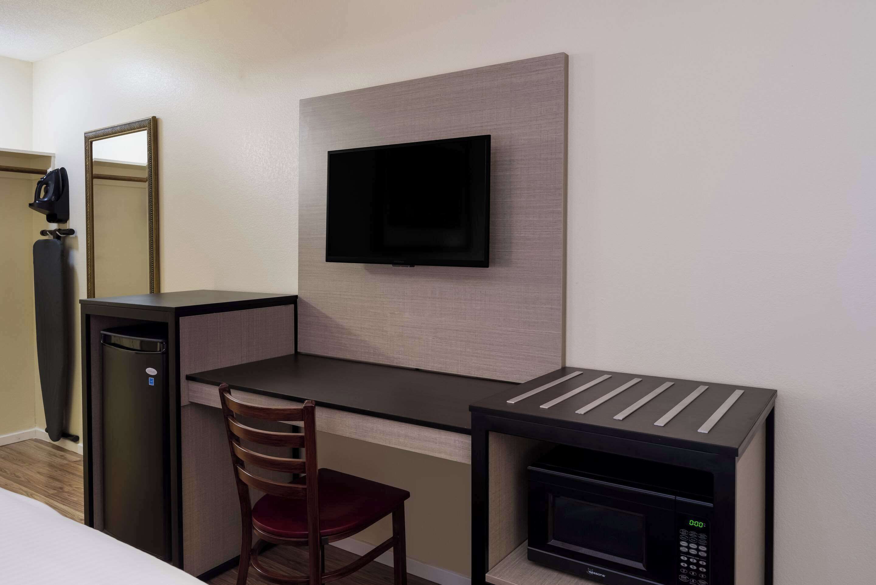 A compact hotel room with a desk, chair, television, and a microwave.