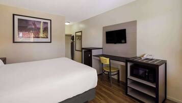 Habitación de hotel con cama, escritorio con silla, microondas, televisión y un cuadro en la pared.
