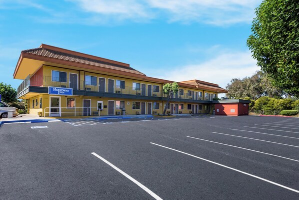 Un motel con un letrero que dice "Rodeway Inn", que presenta una estructura de dos pisos con techo plano, un estacionamiento y un pequeño edificio rojo adyacente.