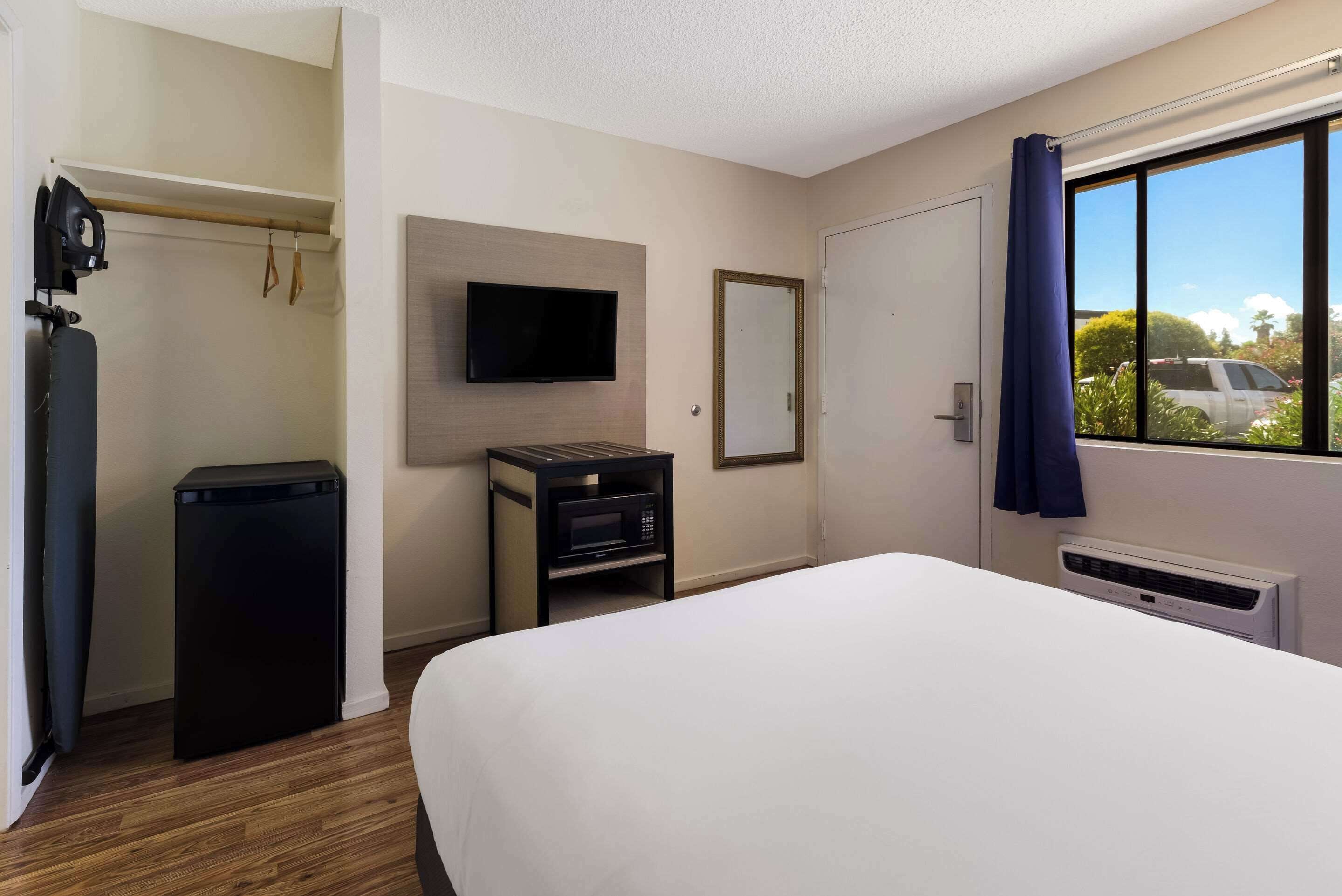 A hotel room with a bed, a TV, a small table with a microwave, a heater, and a view of the outside.