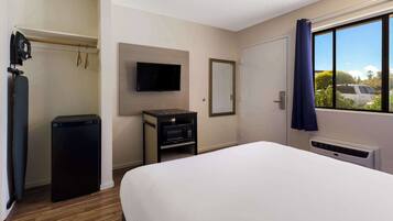 A hotel room with a bed, a TV, a small table with a microwave, a heater, and a view of the outside.