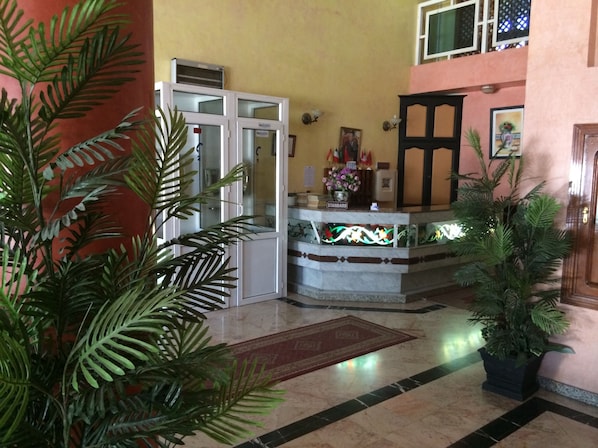 A reception area with a marble counter, a glass door, and potted plants. - Hôtel Marjane (Agadir)