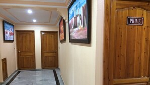 Un pasillo con puertas de madera, piso de mármol y cuadros enmarcados en las paredes.