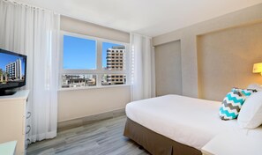 A hotel room with a bed, a TV on a stand, a window with curtains, and a lamp on the wall. - The Wave Hotel Condado (San Juan)