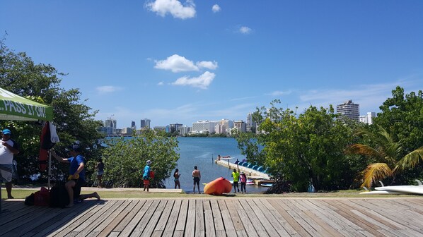 A wooden deck with a city skyline in the background, a clear blue sky, and a calm body of water.