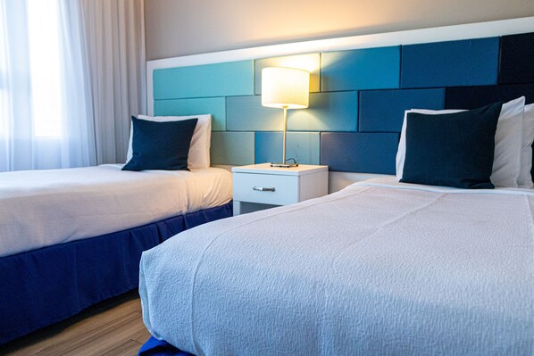Habitación de hotel con dos camas, una mesita de noche con lámpara y cabecera con diseño de panel color turquesa.