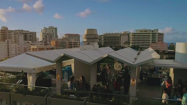 Un bar en la azotea con varias sombrillas blancas, una zona de bar y vistas del horizonte de la ciudad.
