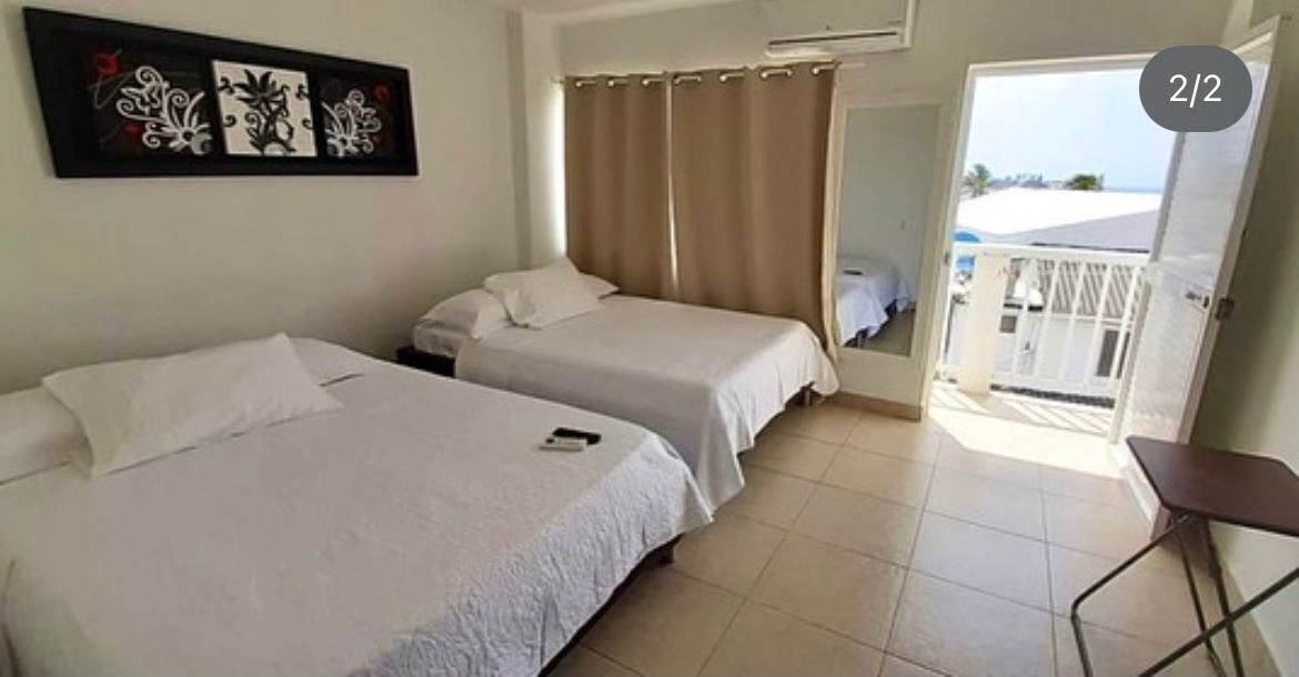 Ein Zimmer mit zwei Betten, einem Sessel, einem Vorhang und einer Tür zum Balkon.
