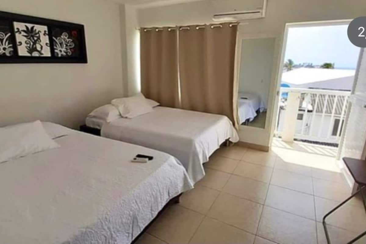 A room with two beds, a chair, a curtain, and a door leading to a balcony.