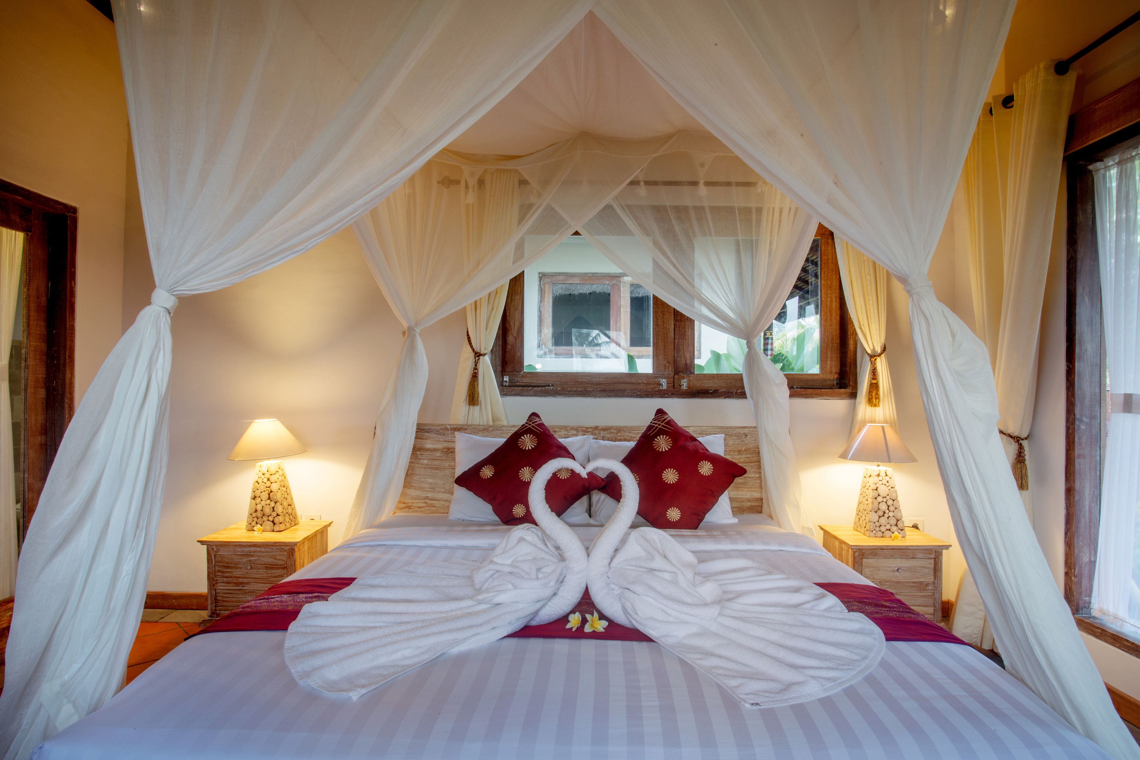 Een hotelkamer met een bed, hemelbed, kussens en nachtlampjes.