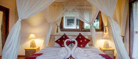 A hotel room with a bed, canopy, pillows, and bedside lamps.