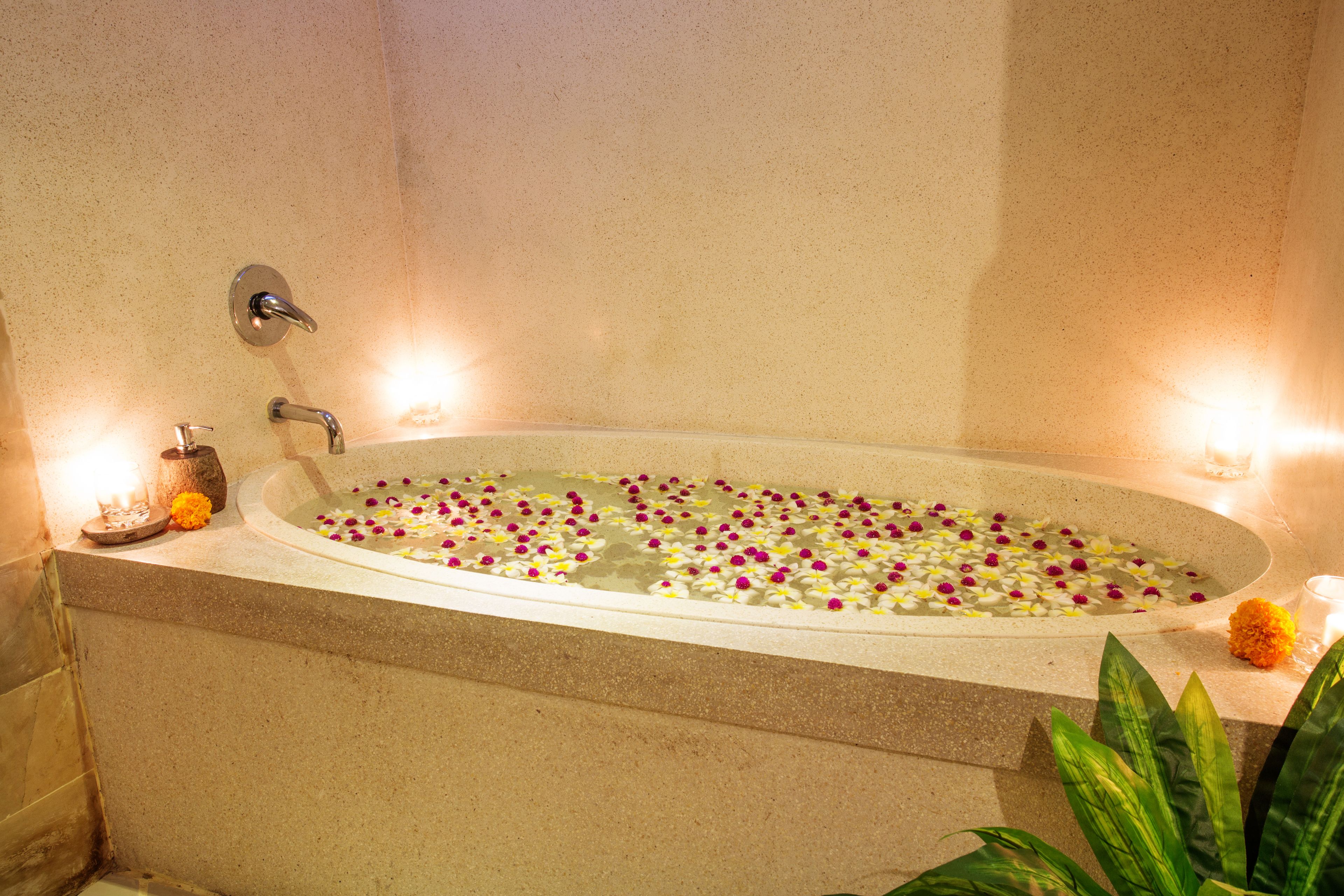 Una bañera llena de agua y pétalos de flores, con velas y un florero al lado.